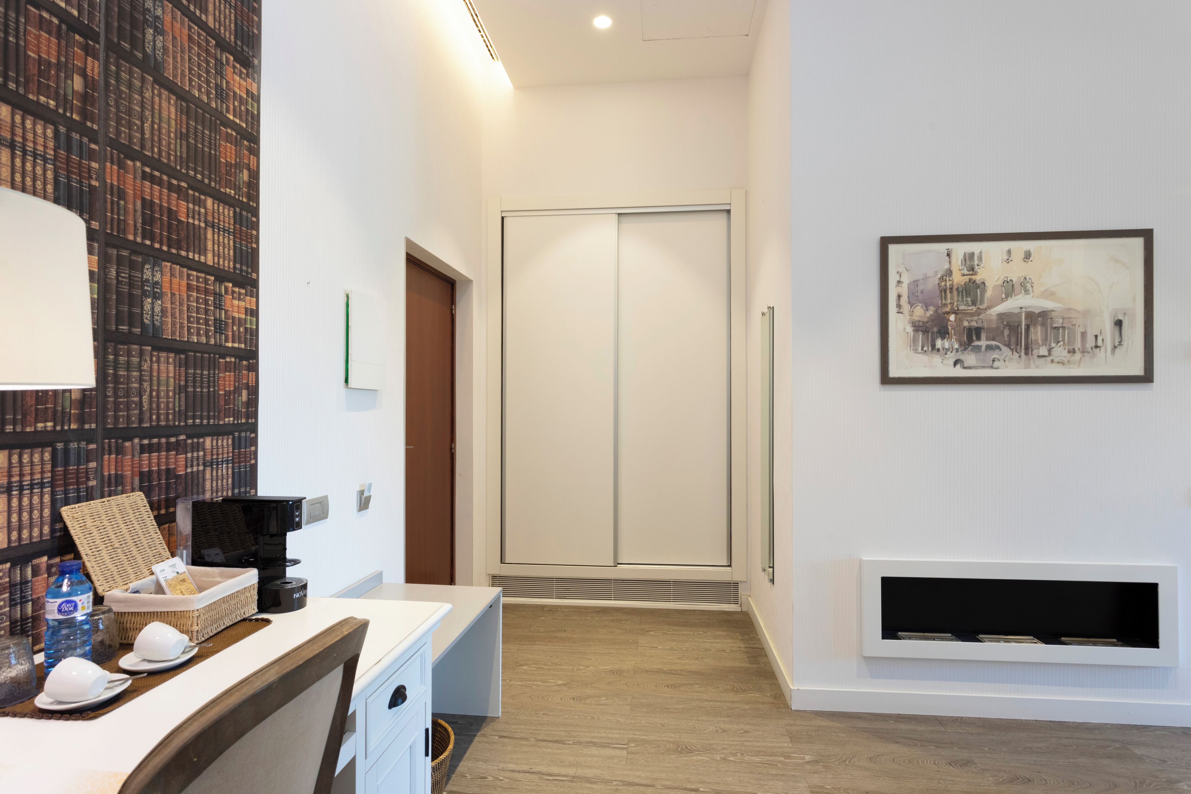 A hotel lobby with a reception desk, a bookshelf, a sliding door, a framed painting, and a built-in fireplace.