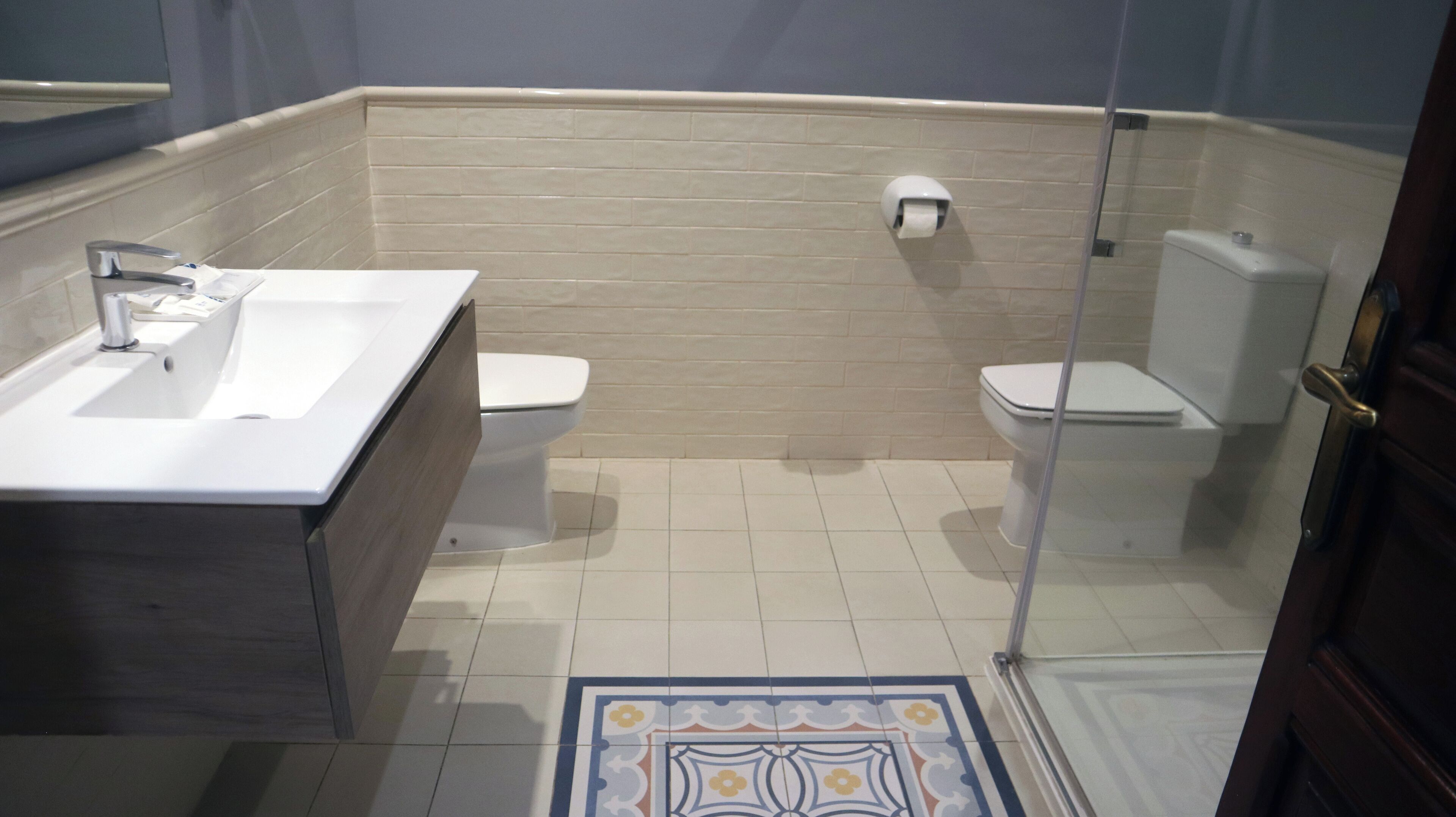 Un baño con lavamanos, dos inodoros y zona de ducha.
