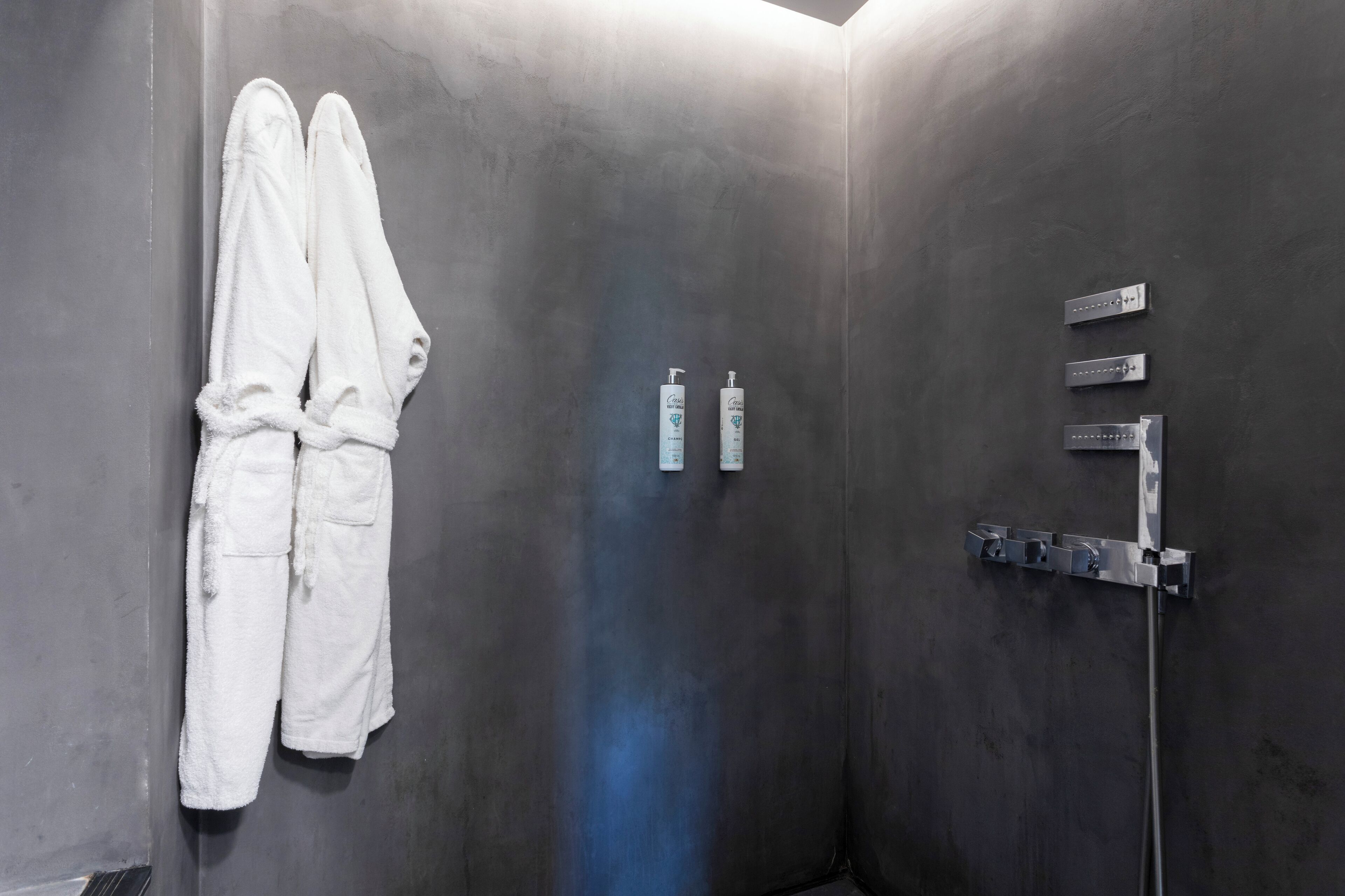 Un baño con pared gris, un perchero con dos toallas blancas y una ducha con grifo y panel de control cromado.