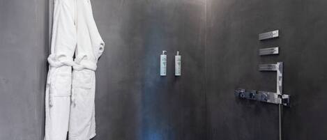 Un baño con pared gris, un perchero con dos toallas blancas y una ducha con grifo y panel de control cromado.