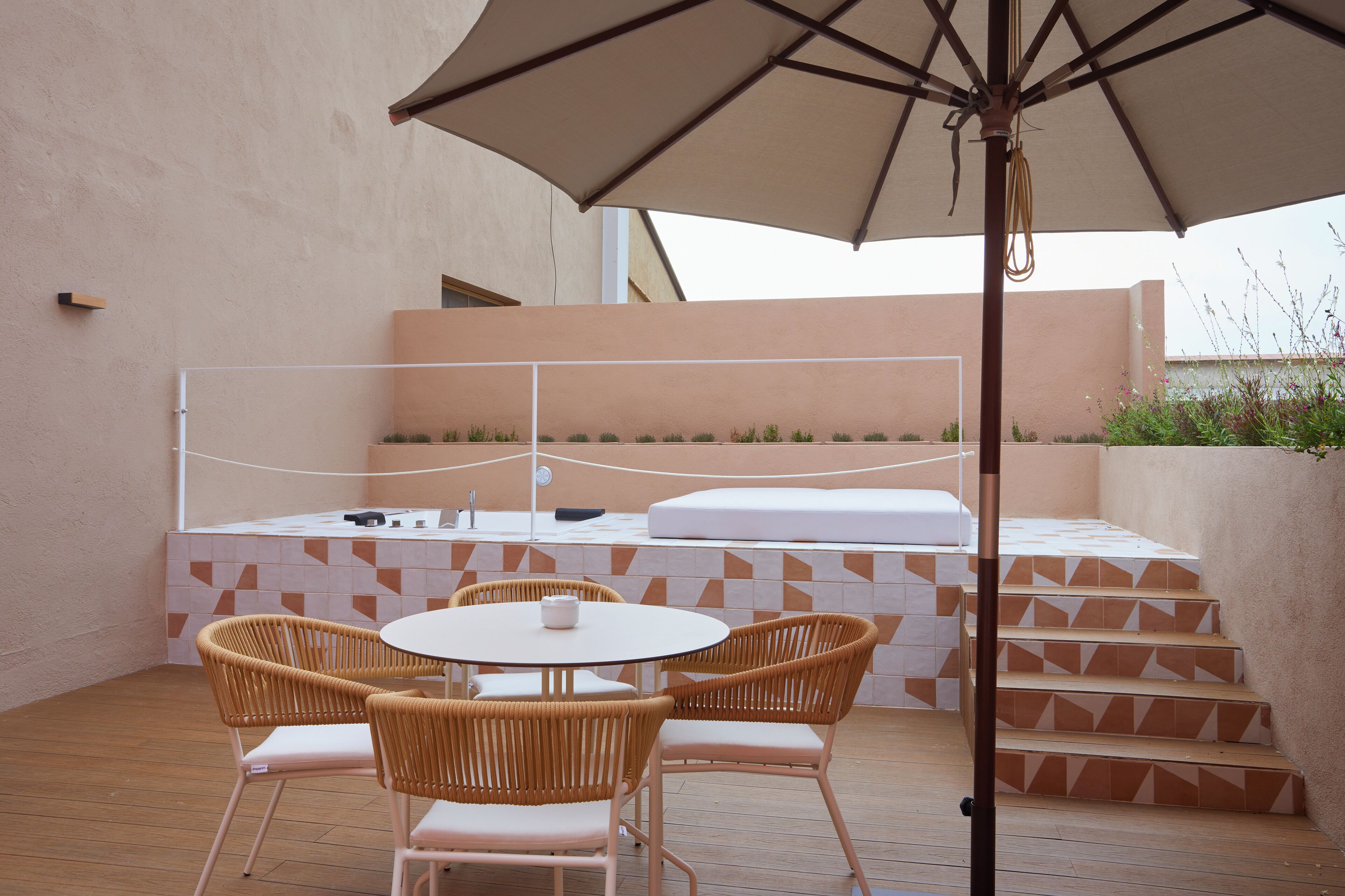Un patio con una mesa redonda, cuatro sillas de mimbre, un paraguas grande y una zona de estar integrada con escalones.