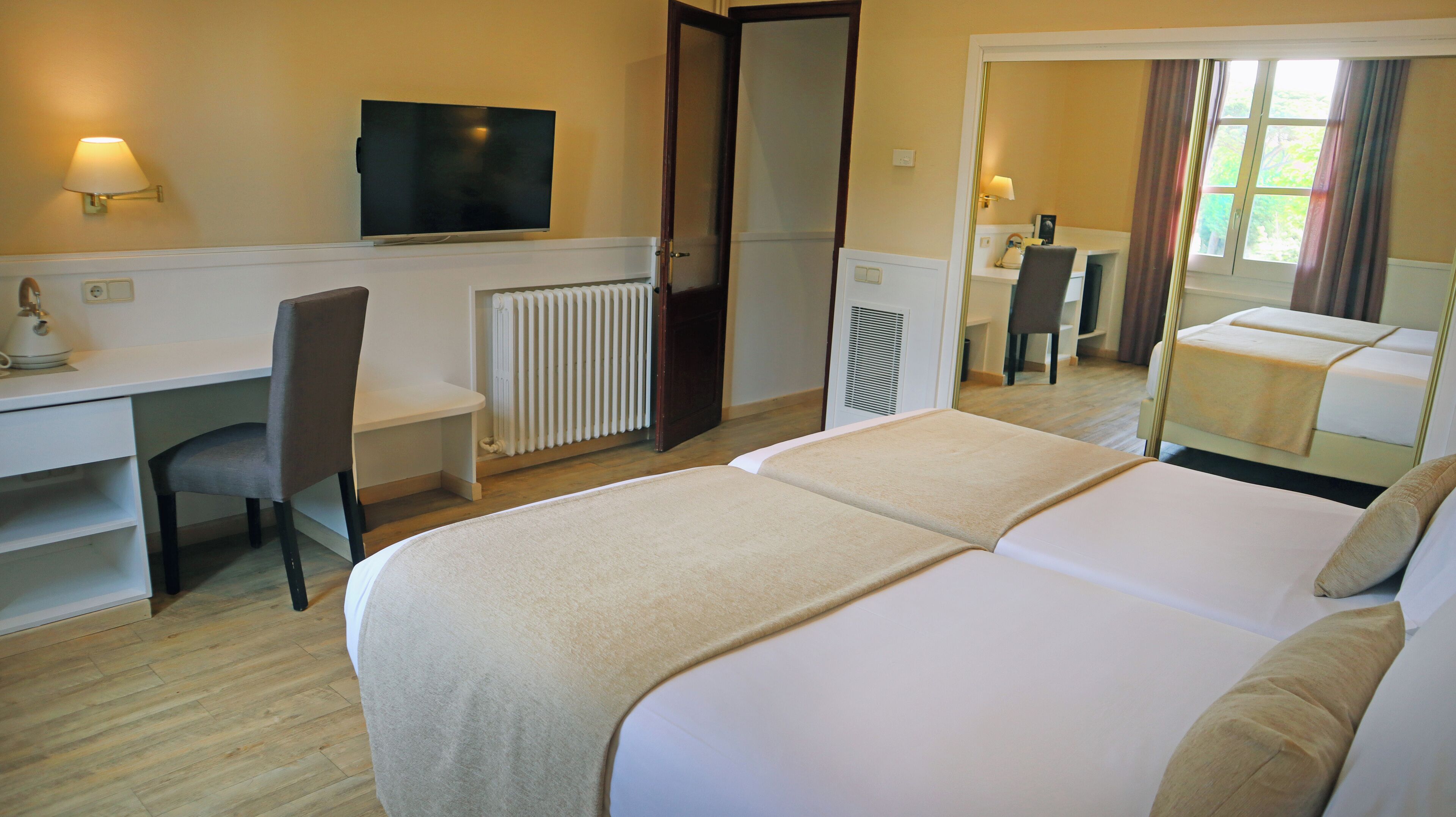 A hotel room with a bed, a desk, a chair, a television, and a radiator.