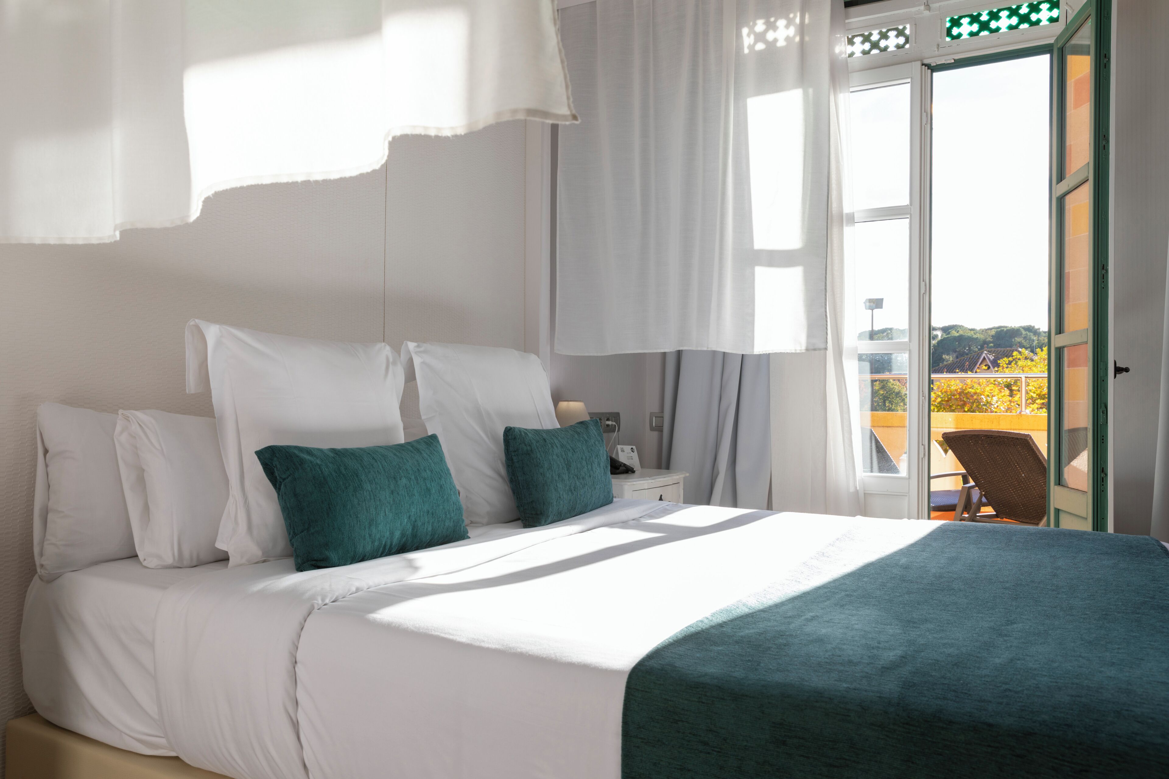 A bedroom with a bed, pillows, a nightstand, and a view of the outdoors through a door.