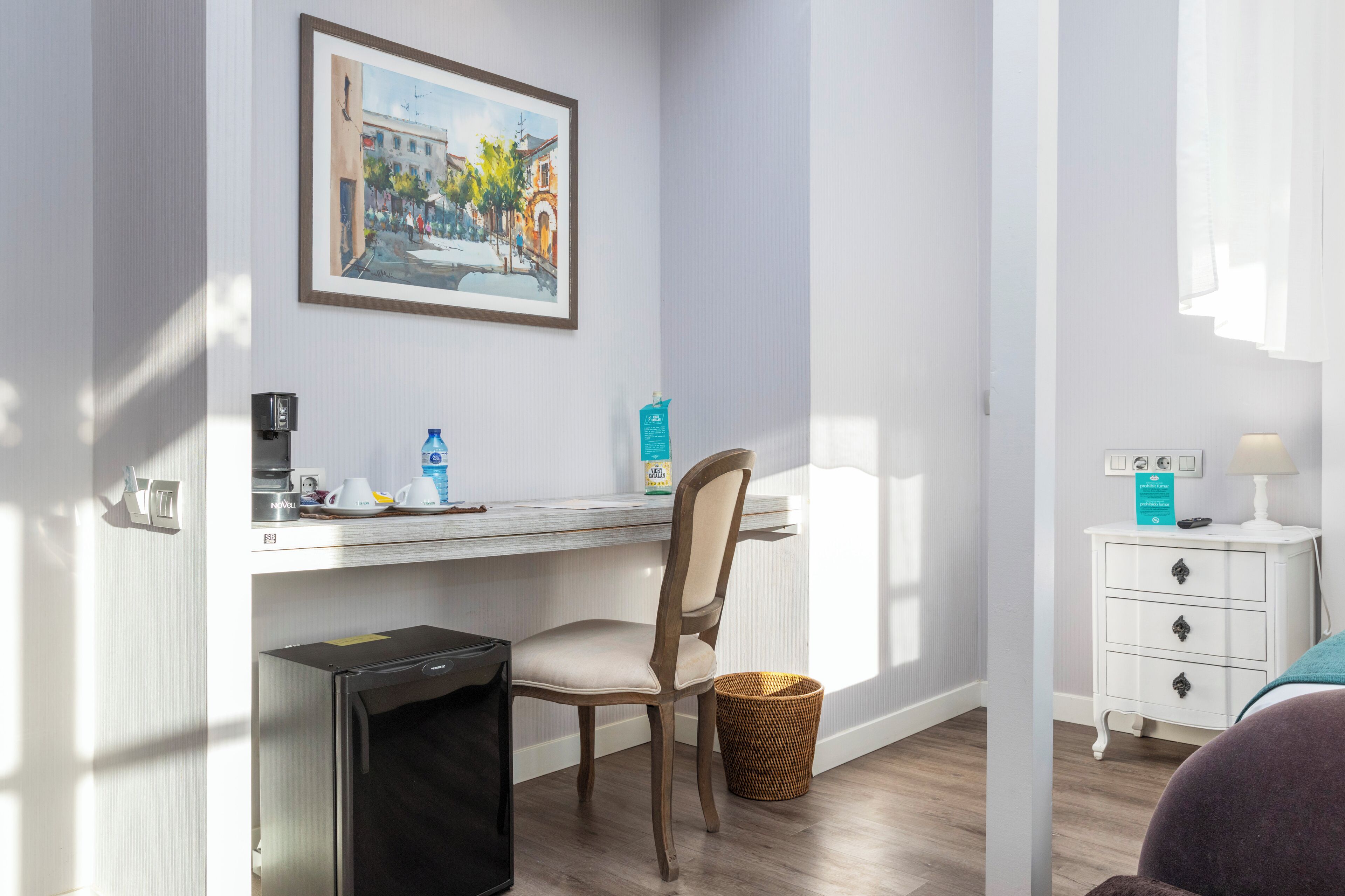Une chambre d’hôtel équipée d’un bureau, d’une chaise et d’une petite table de chevet blanche avec une lampe.
