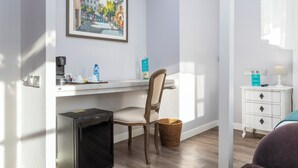 Et hotelværelse med skrivebord, stol og et lille hvidt natbord med lampe.