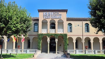 Um edifício histórico com uma placa indicando '1881 Hotel Balneari Vichy Catalan'. Possui uma entrada central com arcos, uma varanda com guarda-corpos decorativos e um telhado em azulejos.