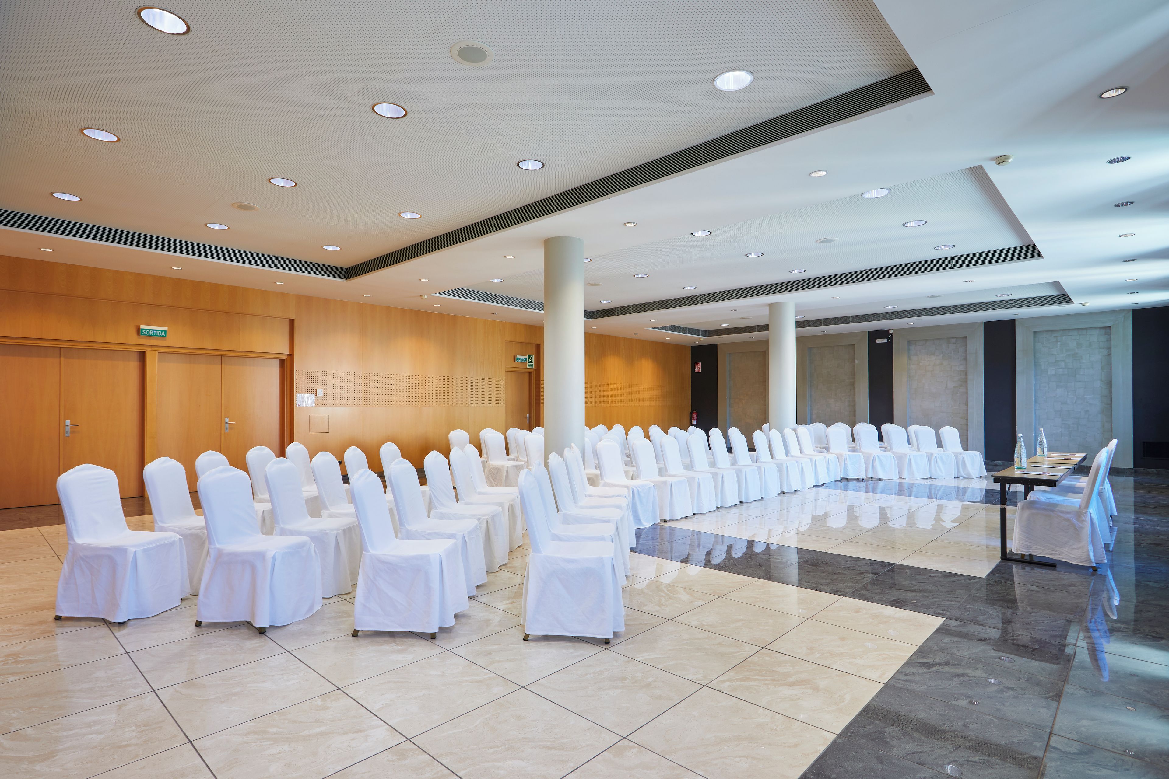 A conference room with rows of chairs and tables, a wooden wall, and a tiled floor.