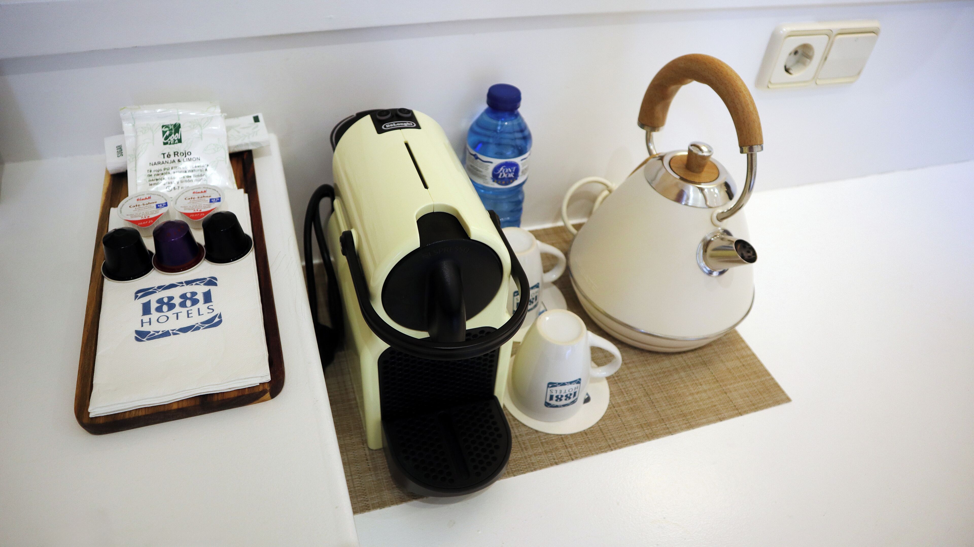 A kitchenette with a coffee maker, tea kettle, and a tray with coffee cups and a water bottle.