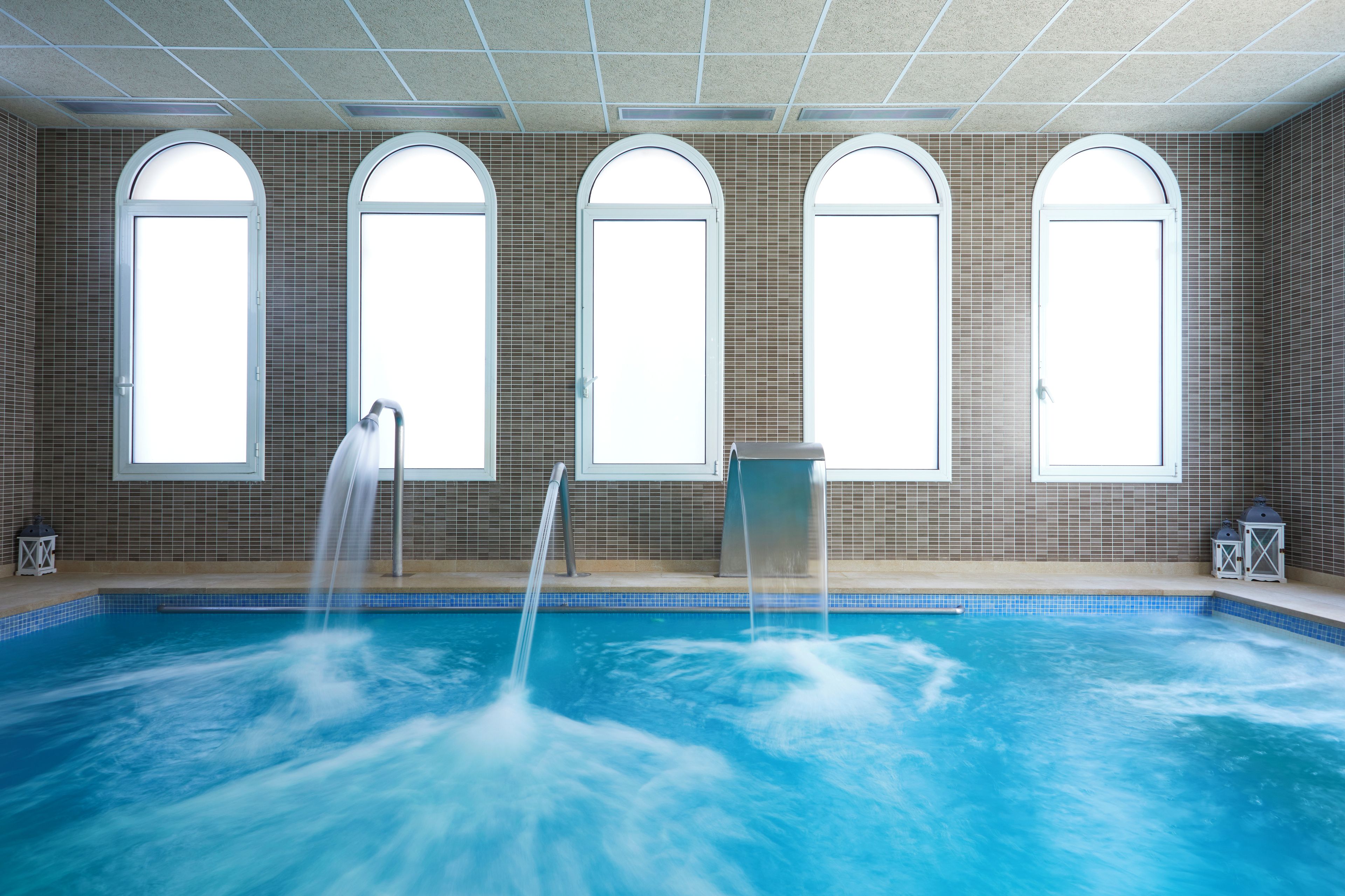 Ein Innenpool mit Wasserspiel, Bogenfenstern und Fliesenwänden.