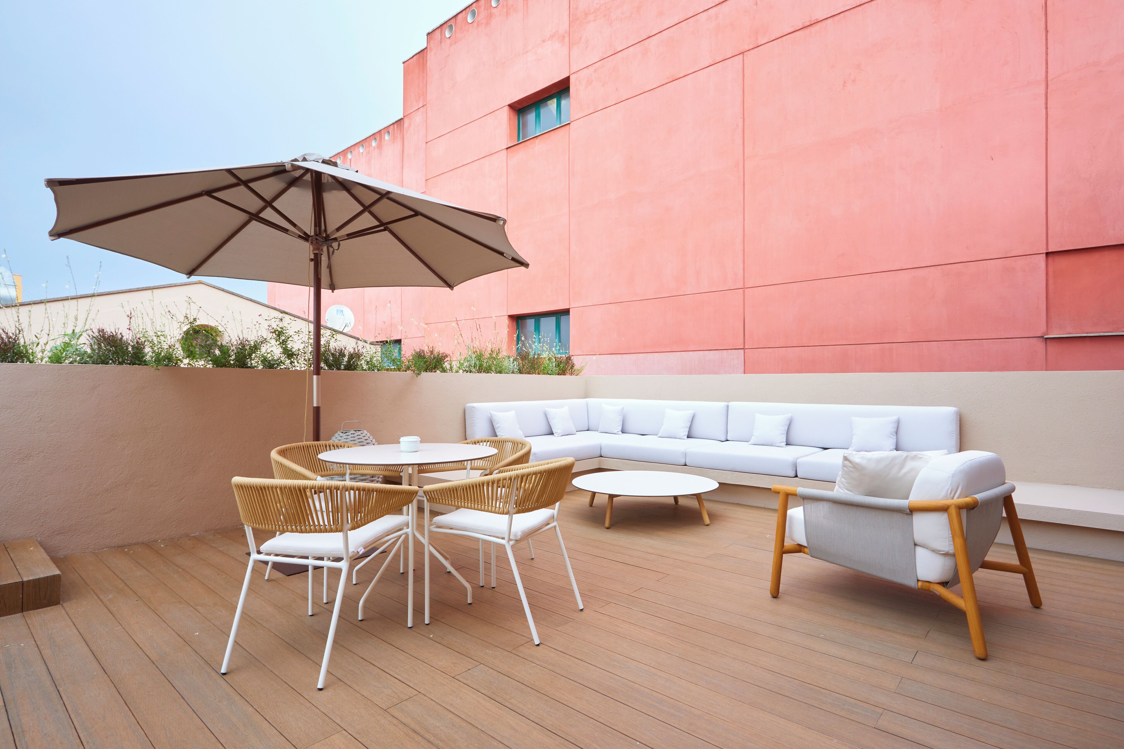 A rooftop terrace with a white sofa, wicker chairs, a round table, and a large umbrella.