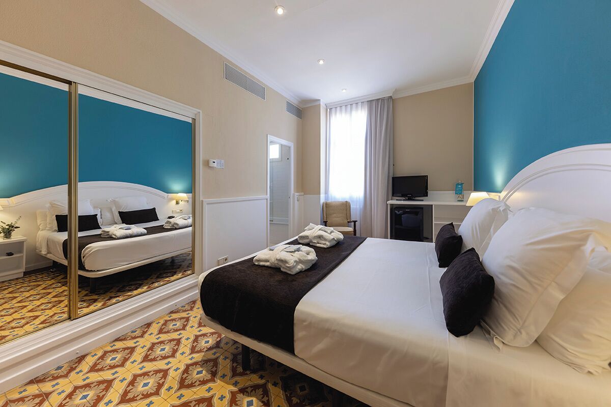 A hotel room with a large bed, a mirror, a desk with a computer, and a television.