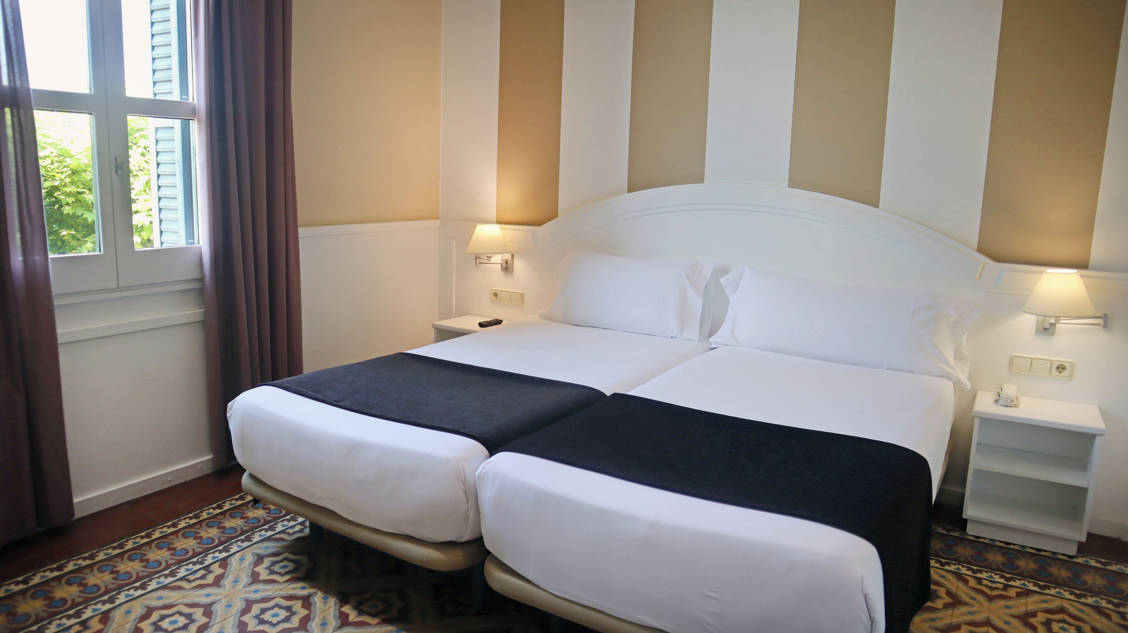 A double bed with two pillows, a bedside table with a lamp, and a nightstand with a phone.