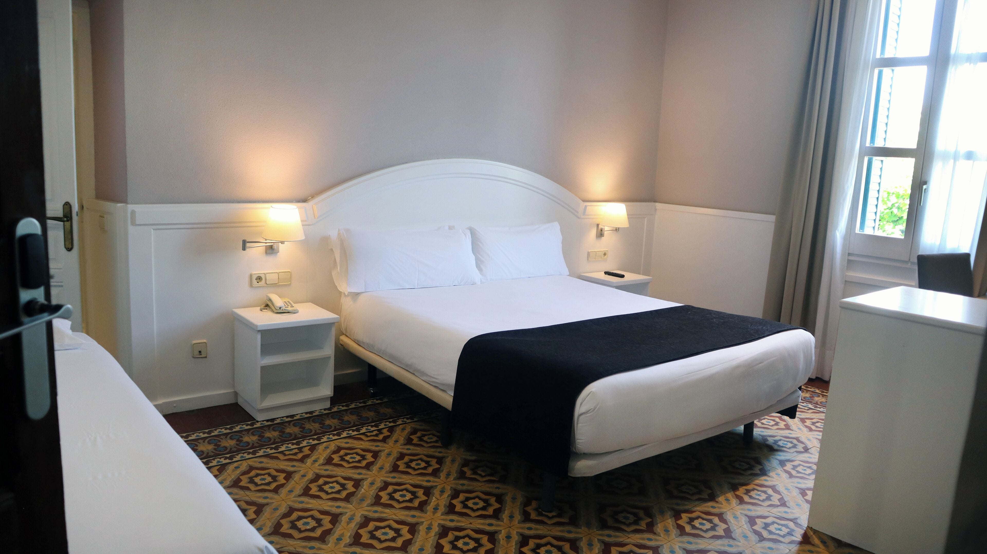 A hotel room with a bed, bedside tables, a telephone, and a window with curtains.