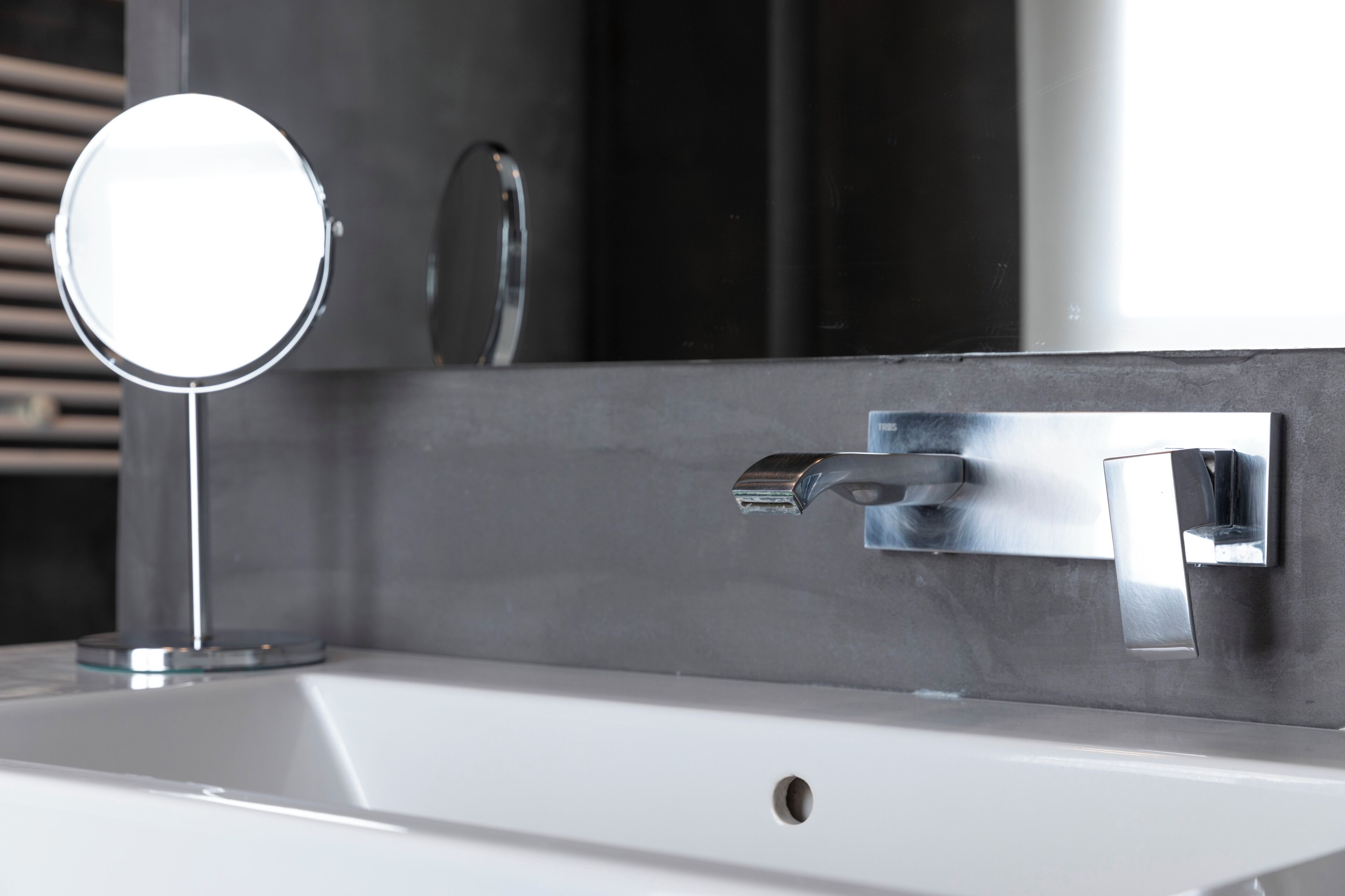 Un lavabo de salle de bain avec un miroir rond, un robinet chromé et un porte-serviettes fixé au mur.
