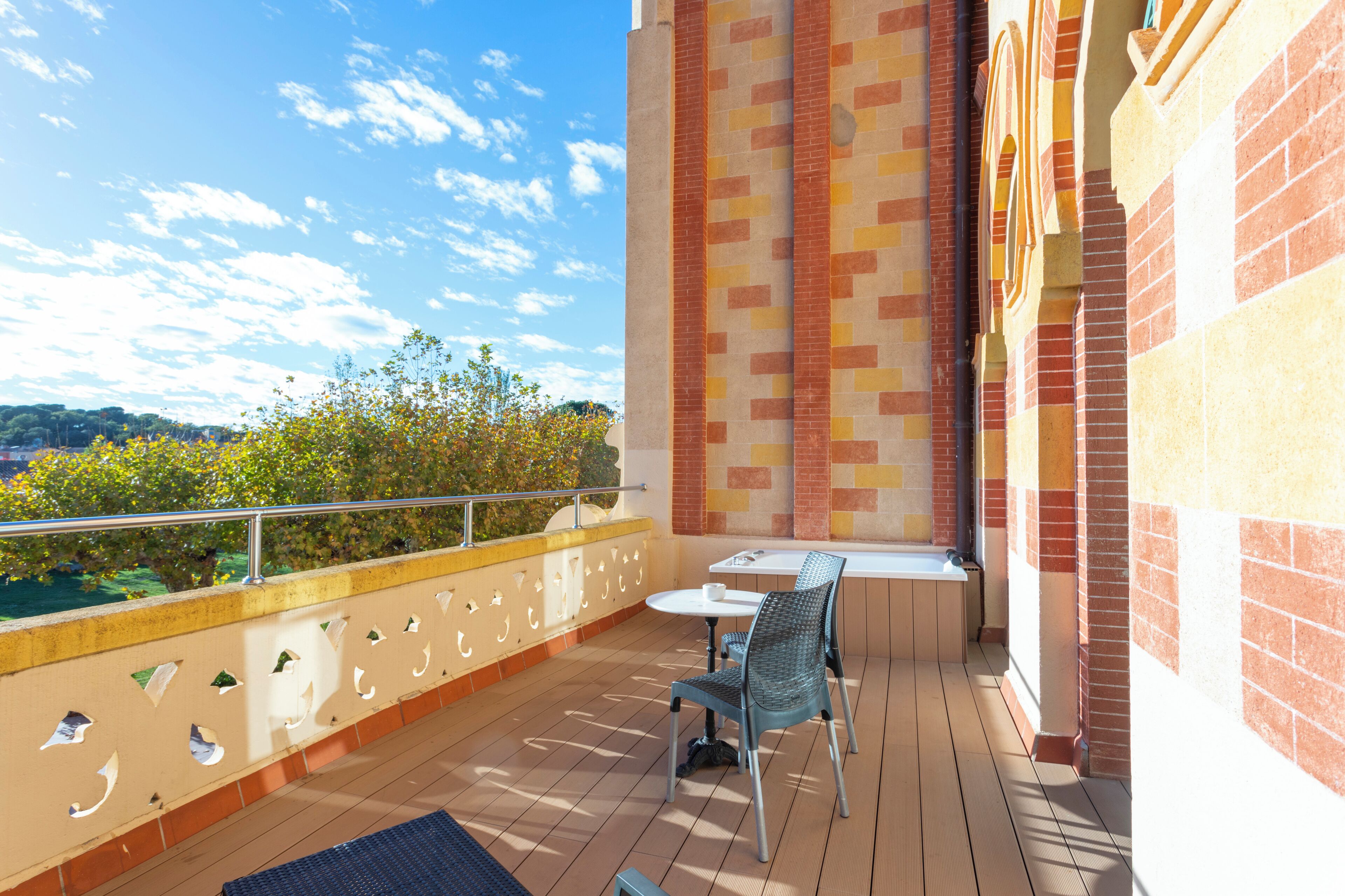 Un balcón con mesa y sillas, vista al cielo y un muro de ladrillo.