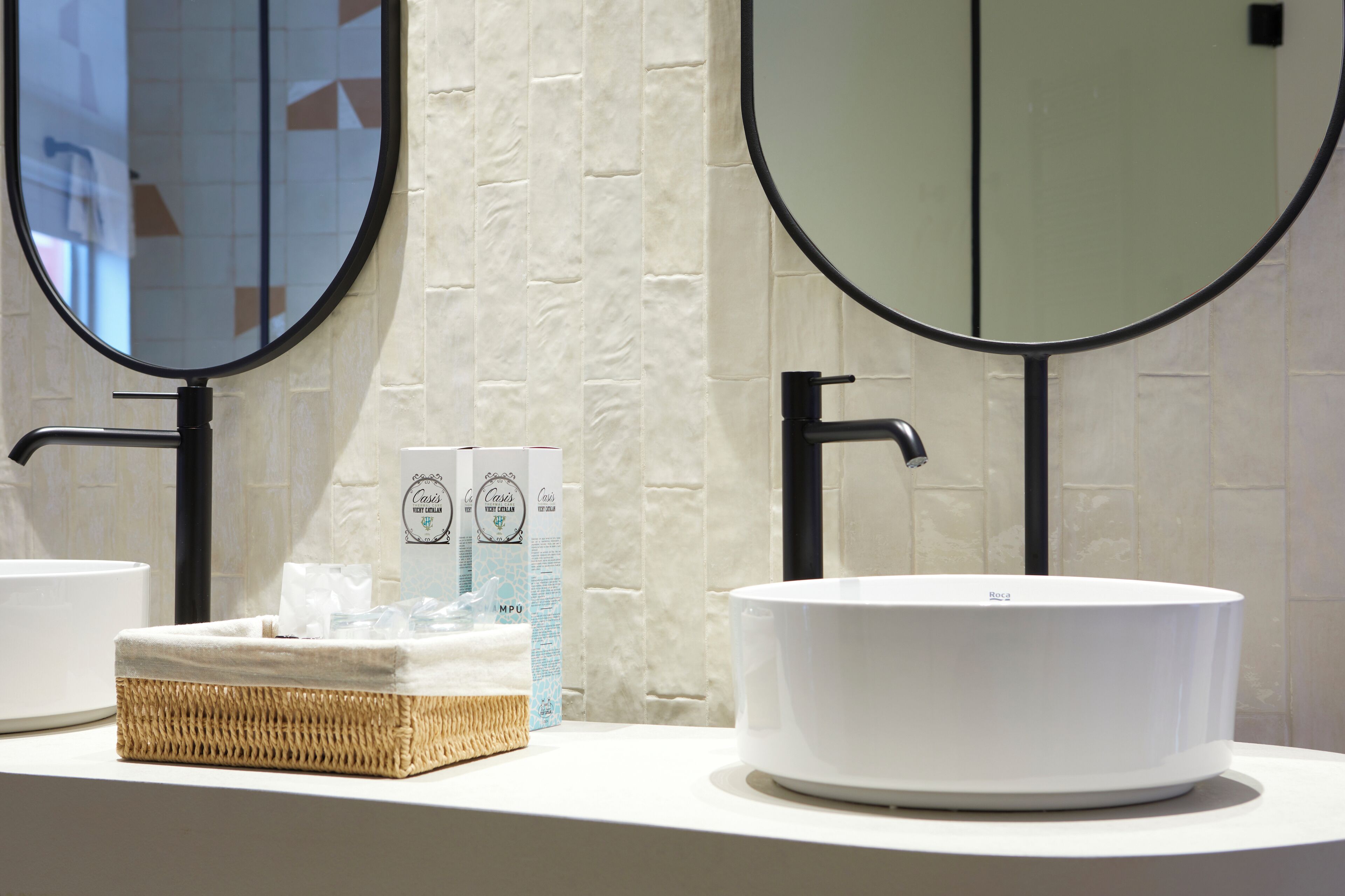 Une salle de bain avec deux miroirs ronds, un lavabo blanc et un panier en osier contenant des articles de toilette.