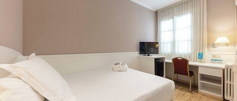 Habitación de hotel con cama, escritorio, silla, televisor y ventana con cortinas.