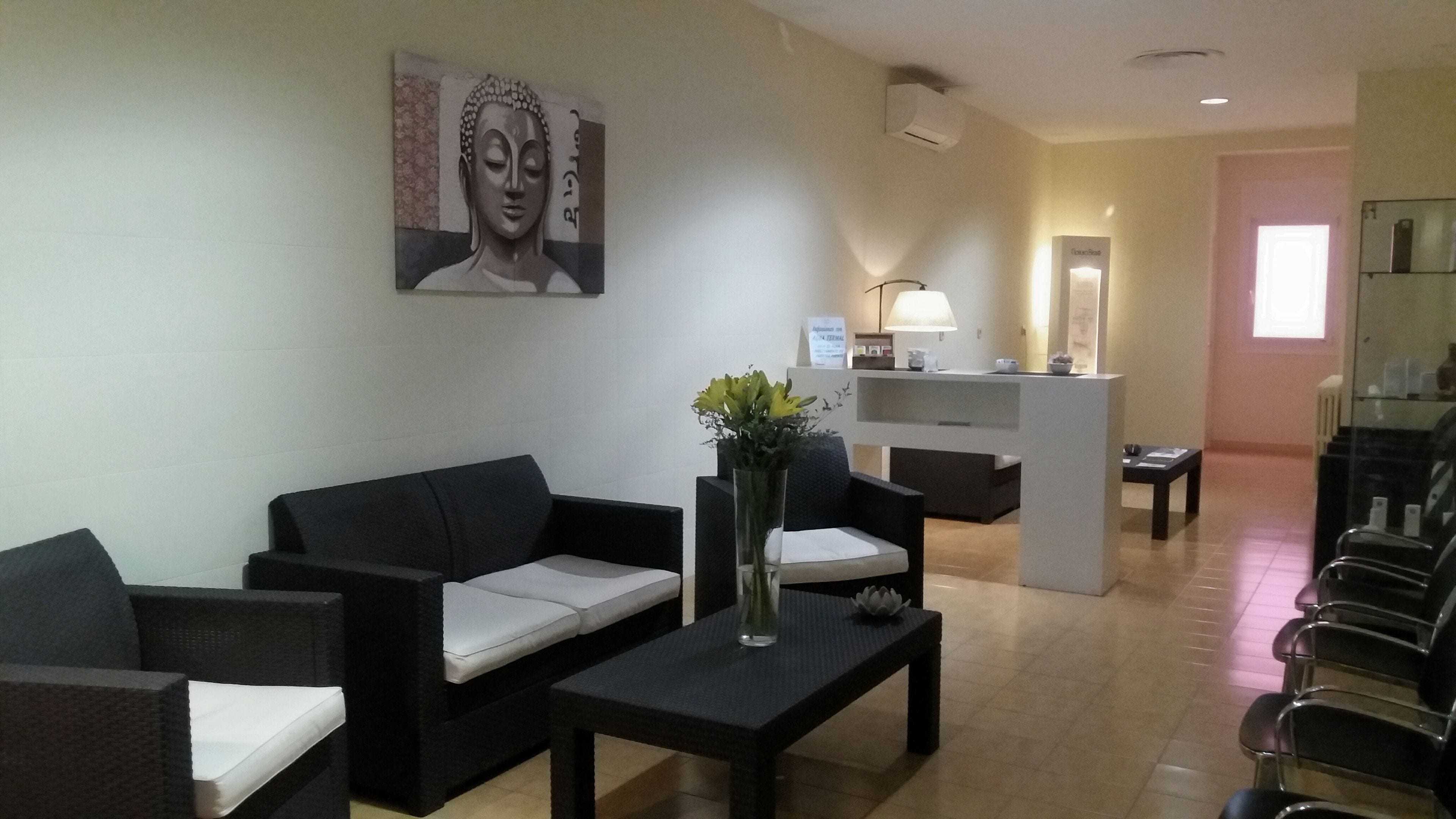 Uma área de recepção com balcão, sala de espera com cadeiras, um sofá, mesa de centro e um vaso com flores.