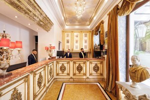 A grand lobby with marble flooring, ornate gold detailing, and a large chandelier.