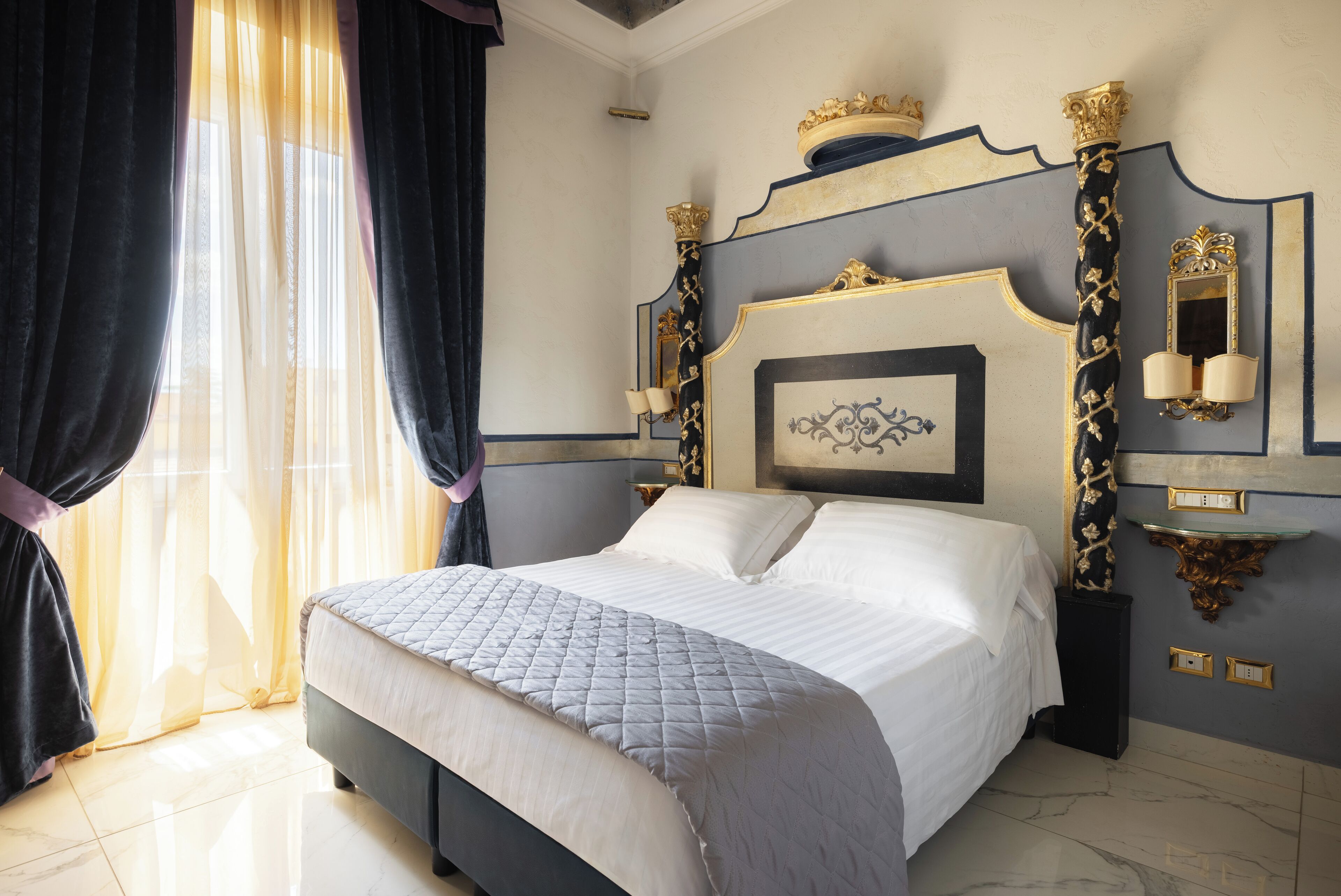 Une chambre à coucher avec un grand lit, une tête de lit ornée d’éléments décoratifs, une table de chevet et un luminaire fixé au mur.