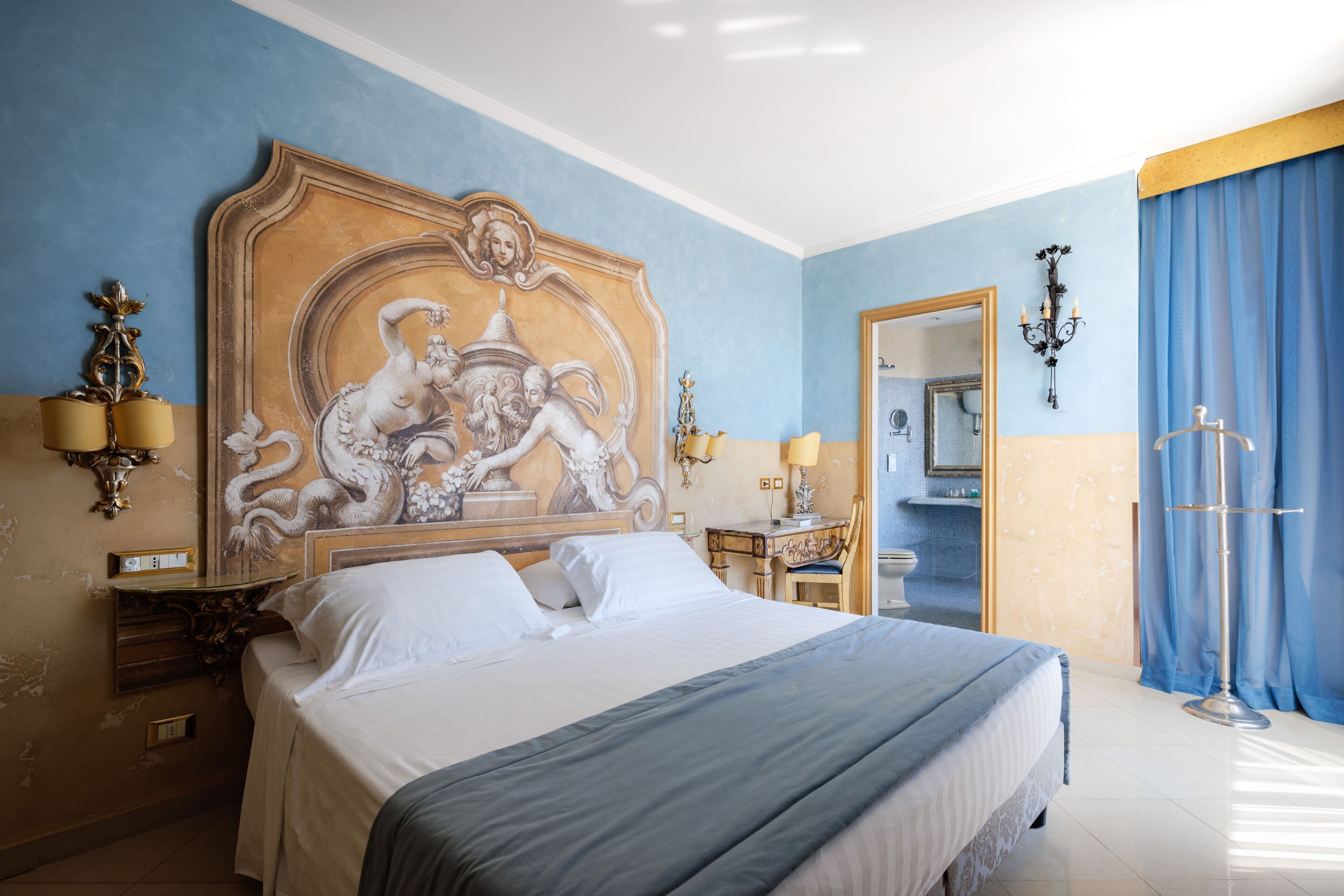 Een hotelkamer met een groot bed, een kaptafel, een bureau en een kroonluchter.