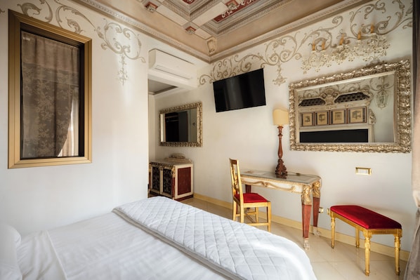A hotel room with a bed, a desk, a chair, a TV, and ornate wall decorations. - ROMANICO PALACE LUXURY HOTEL & SPA (Rome)