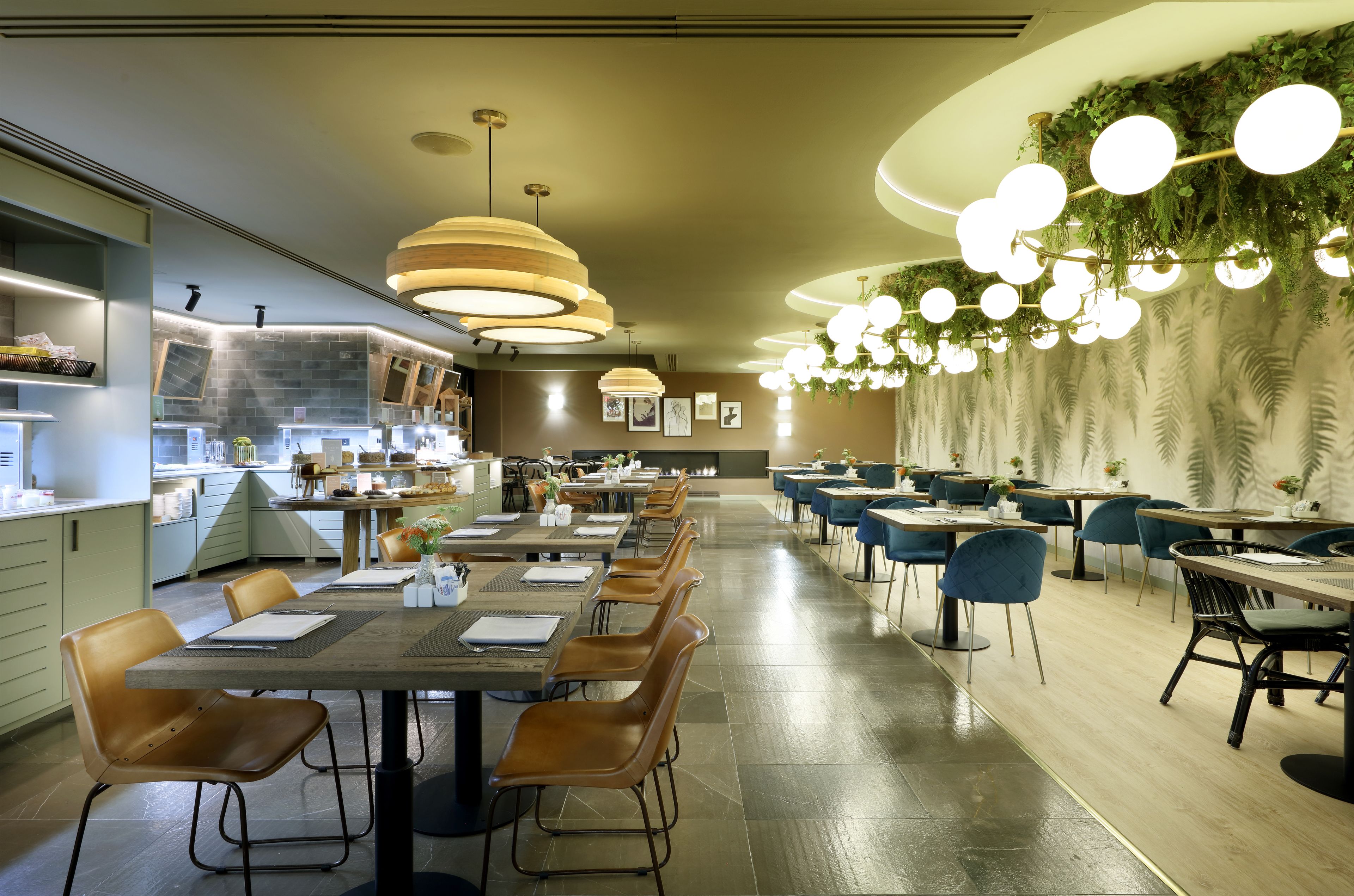 A modern restaurant with long communal tables, individual booths, and a variety of lighting fixtures.