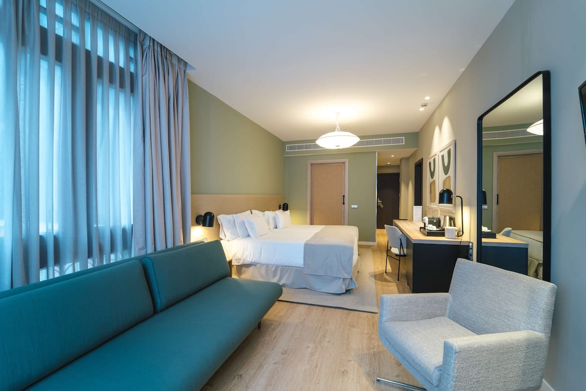 Een hotelkamer met een bed, een bank, een stoel, een bureau en een spiegel.