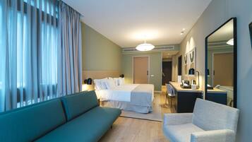 Habitación de hotel con cama, sofá, sillón, escritorio y espejo.