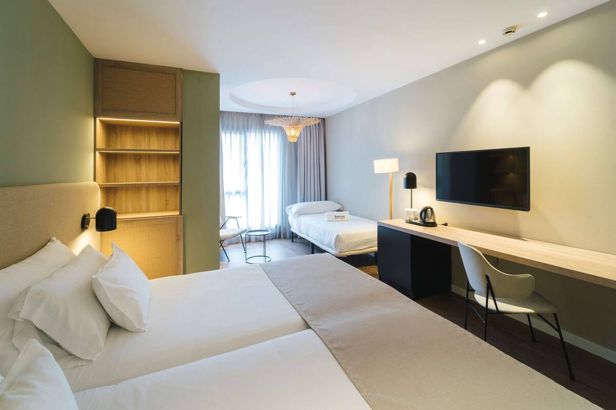 Een hotelkamer met een groot bed, een bureau met stoel, een televisie en een kleine tafel met lamp.