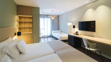 Habitación de hotel con una cama grande, un escritorio con silla, un televisor y una mesita de noche con lámpara.