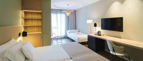 A hotel room with a large bed, a desk with a chair, a TV, and a small table with a lamp.