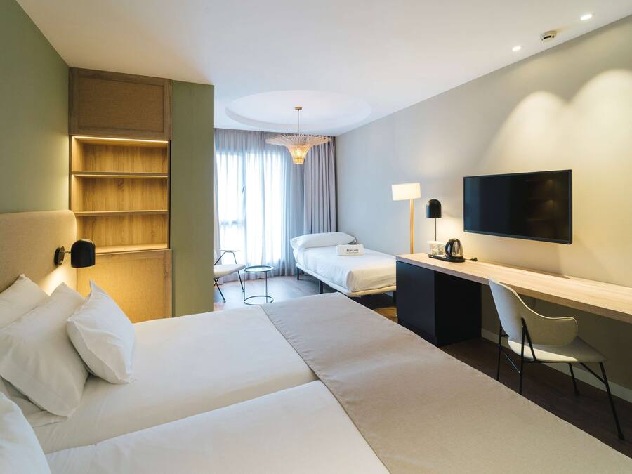 Habitación de hotel con una cama grande, un escritorio con silla, un televisor y una mesita de noche con lámpara.