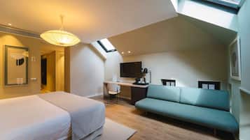 A modern hotel room with a loft bed, a desk, a sofa, and a skylight.