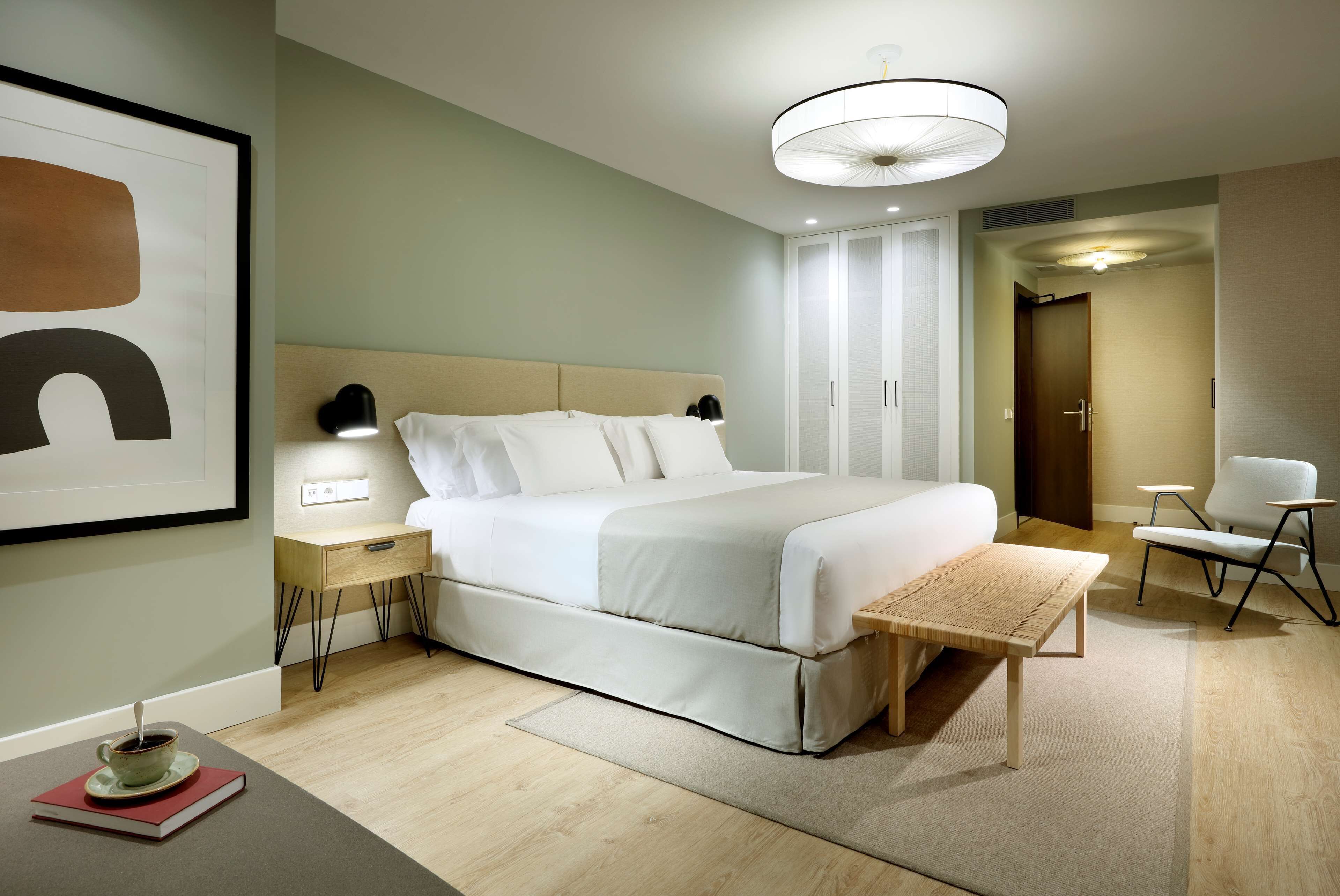 Habitación de hotel moderna con una cama grande, mesitas de noche, lámparas de noche, una pequeña mesa y una silla.