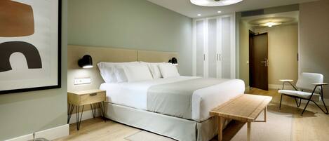 Een moderne hotelkamer met een groot bed, nachtkastjes, een bedlampje, een klein tafeltje en een stoel.