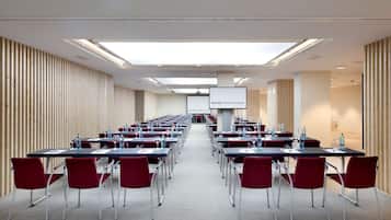 A conference room with rows of tables and chairs, a projector screen, and a wooden slat wall.