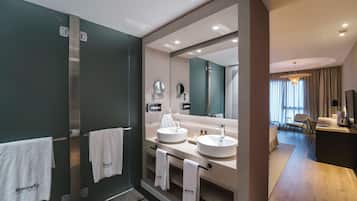 A modern bathroom with two sinks, a large mirror, and a vanity. There are towels hanging on a rack and a shower area visible.