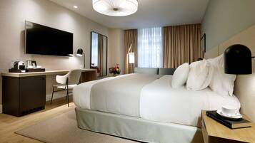 Una habitación de hotel moderna con una cama grande, un escritorio con televisor de pantalla plana, una cafetera y una mesita de noche con un libro y una taza.
