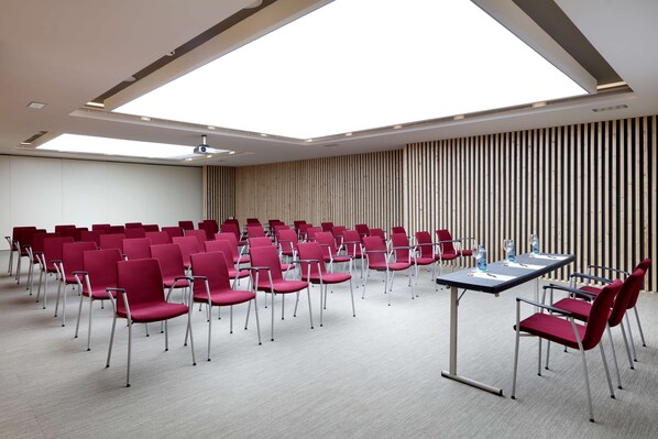 A conference room with rows of red chairs, a long table, and a slanted ceiling with skylights.