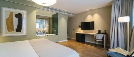 A modern hotel room with a large bed, a desk with a chair, a TV, and a window with curtains.