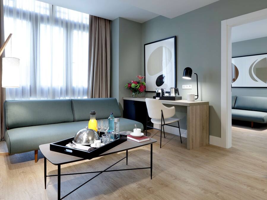 A modern living room with a sofa, a coffee table with a tray, a desk with a lamp, and a chair.