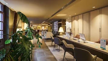 Um saguão de hotel com balcão de recepção, área de estar e uma grande planta.