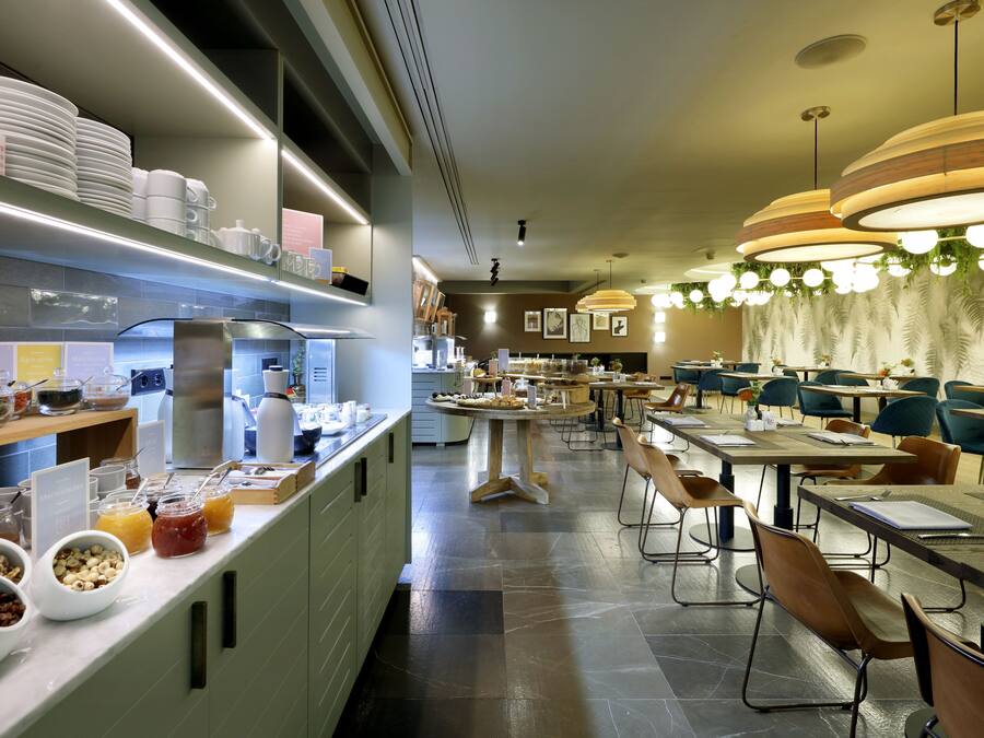 Un comedor moderno con varias mesas y sillas, un mostrador de buffet con diferentes opciones de comida e iluminación colgante.