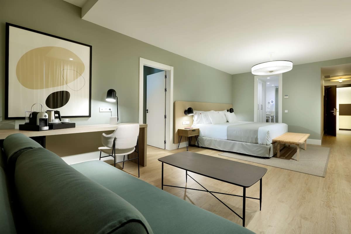 Een moderne hotelkamer met een bed, een bureau, een stoel, een bank en een koffiezetapparaat.