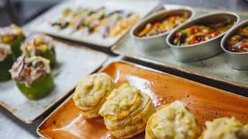 Una mesa de bufé con diversos alimentos, incluyendo pimientos rellenos, pasteles y una variedad de platos en recipientes de metal.