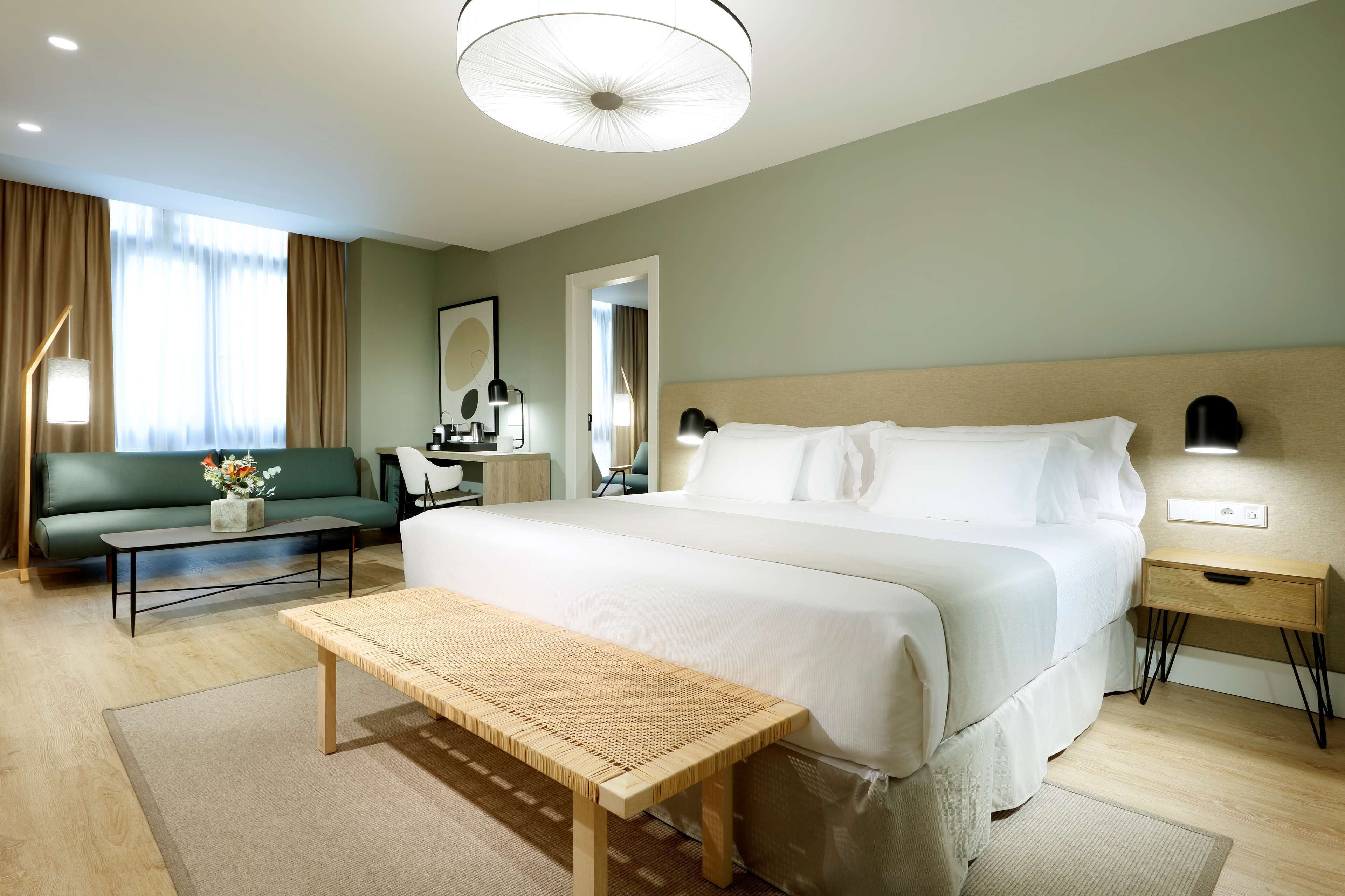Una habitación de hotel con una cama grande, una banca de madera, un sofá, un escritorio y una lámpara.