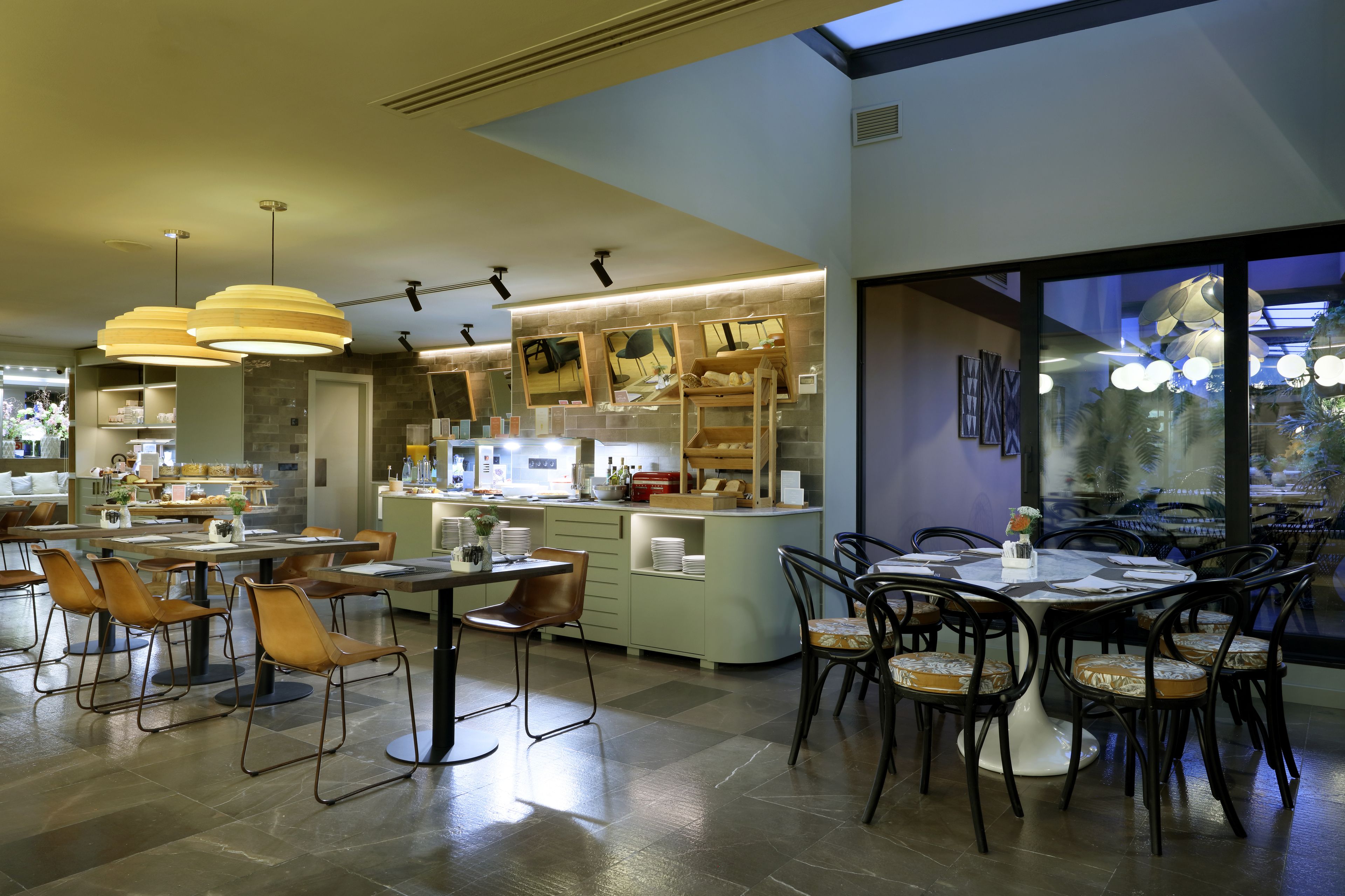 Un restaurant moderne doté de plusieurs espaces de restauration, d’une cuisine ouverte et de grandes fenêtres offrant une vue sur la ville.