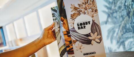 Una mano sostiene un folleto con motivos florales y tropicales, sobre una superficie de madera.