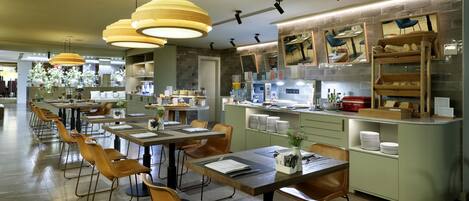A modern restaurant with long communal tables, wooden chairs, and pendant lighting.